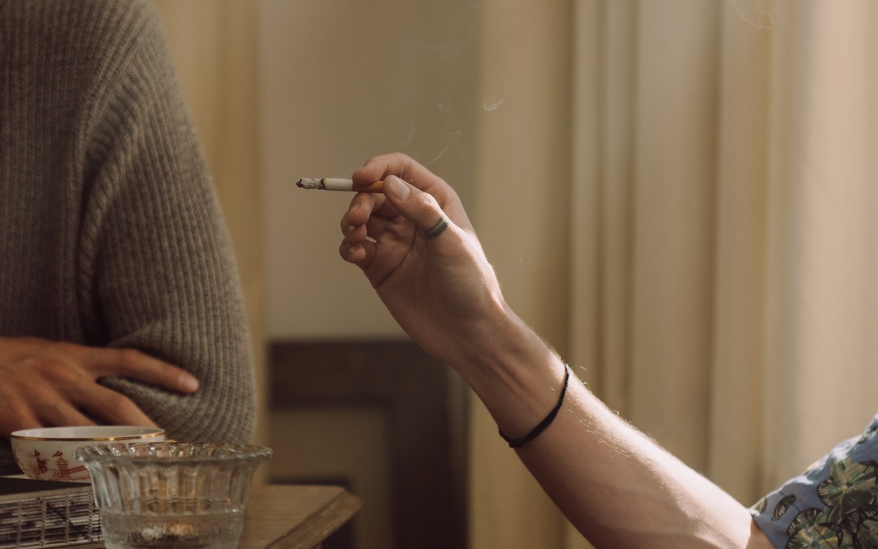 Kobieca dłoń trzymająca zapalonego papierosa, z którego unosi się dym