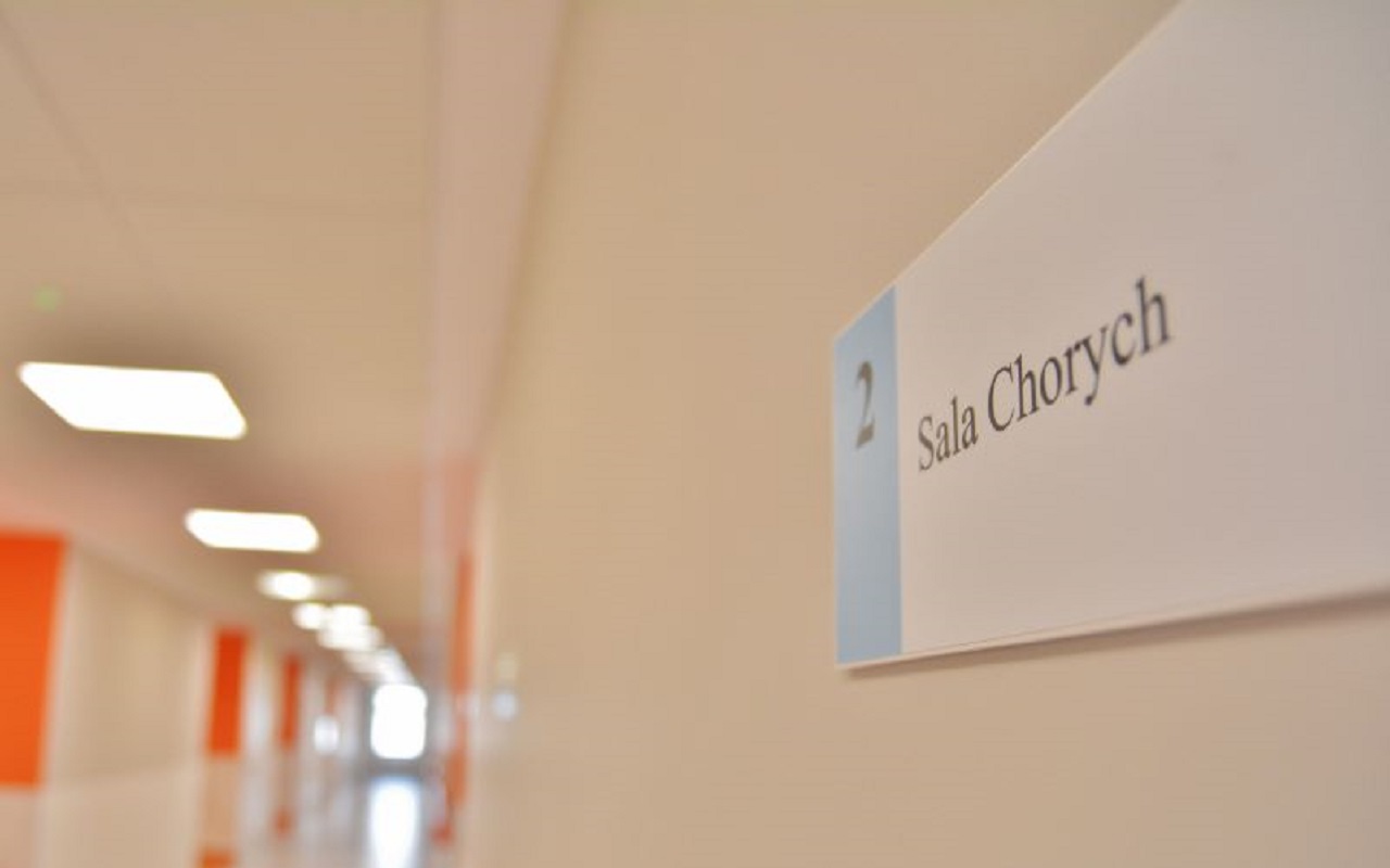 Szpitalny korytarz, na pierwszym planie widoczna tabliczka z numerem sali chorych
