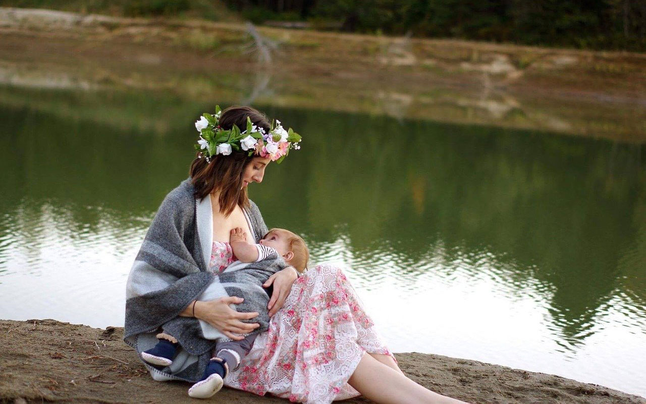  młoda kobieta siedzi z małymi dzieckiem przy piersi