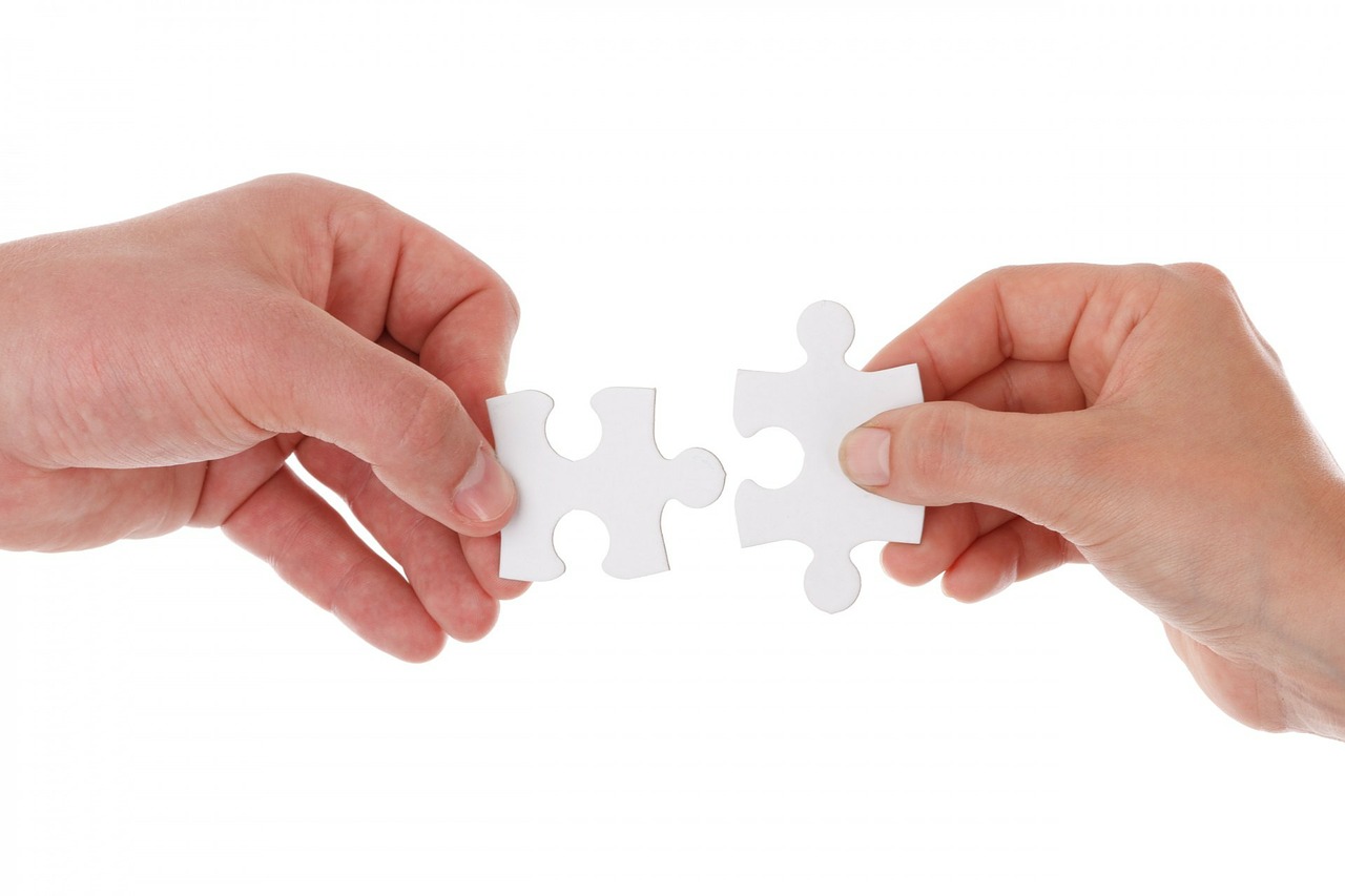 Dwie osoby trzymają w ręce puzzle próbując je połączyć