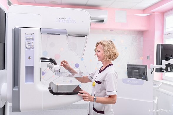 urządzenie do badania piersi mammograf przed którym stoi pielęgniarka ale nie wykonuje badania