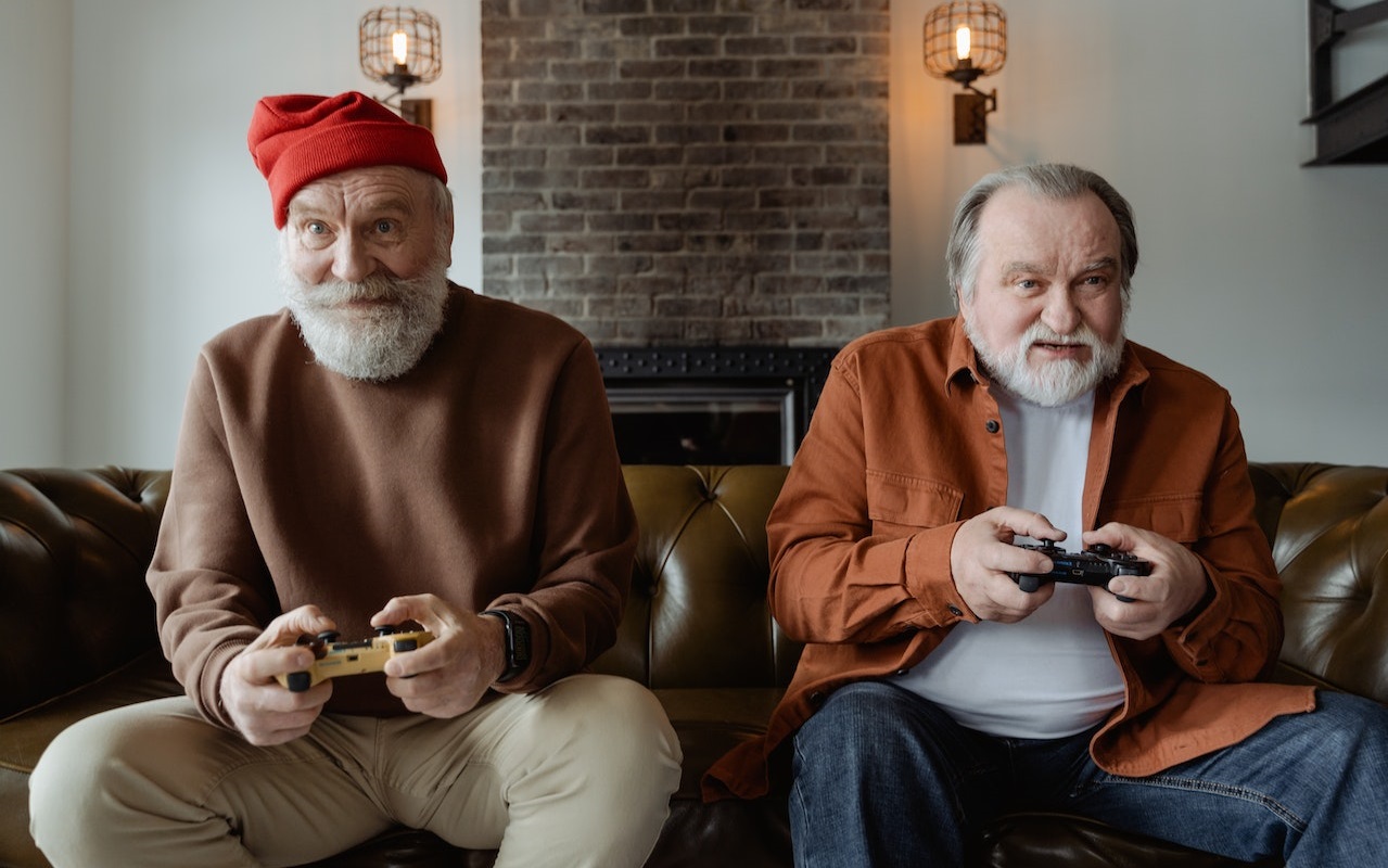 Dwóch starszych panów siedzących na sofie z kontolerami do gry w dłoniach